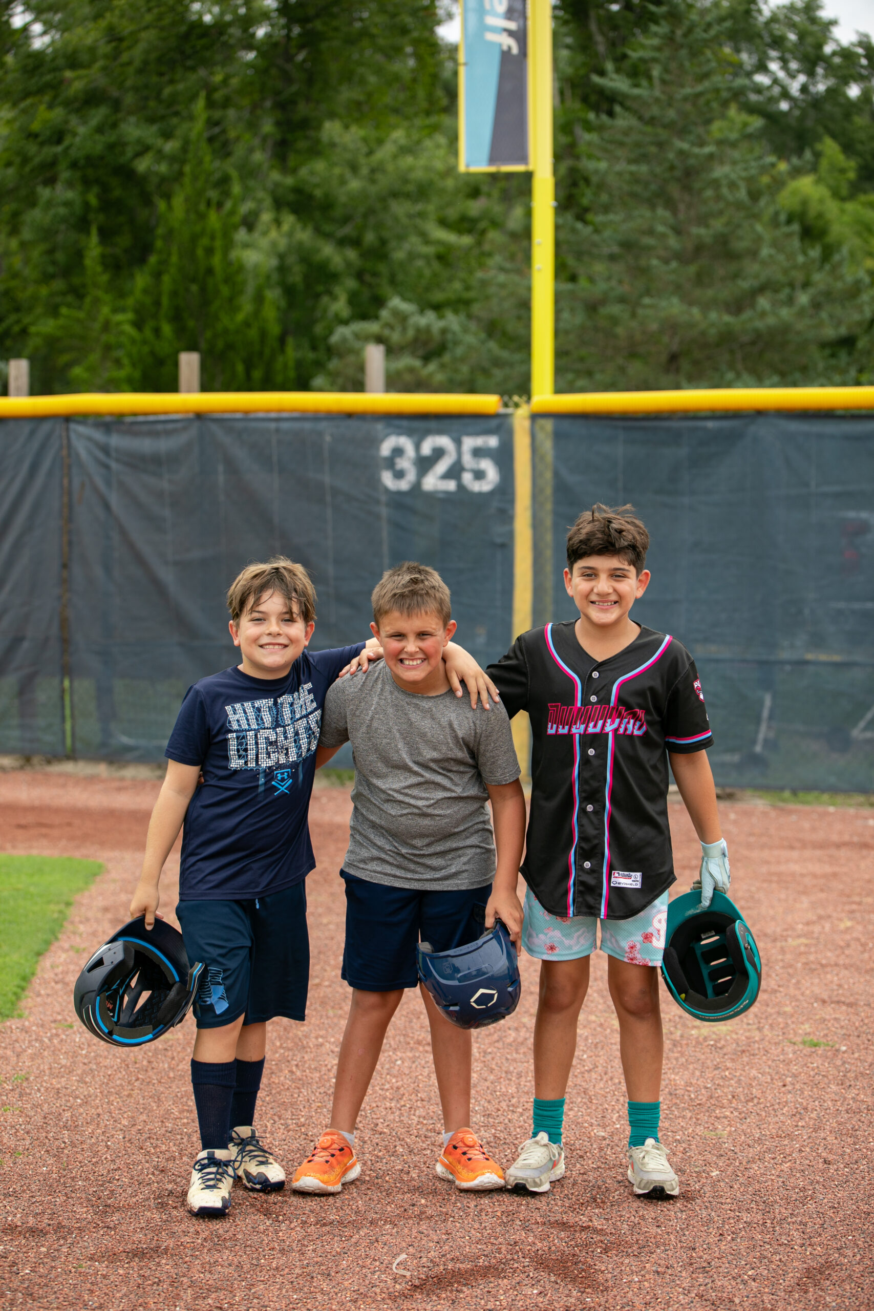 Three campers posing for a photo on UNF's baseball field at Osprey Baseball Camp.